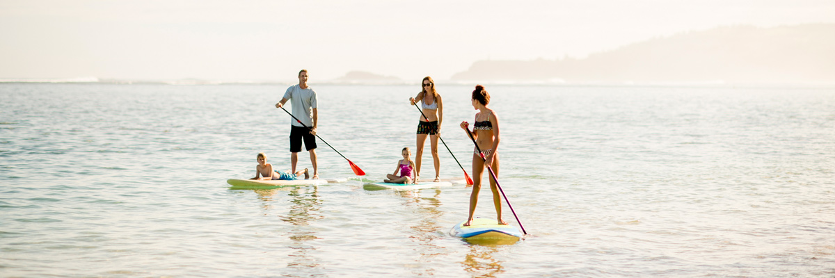 La familia y su au pair en la playa haciendo paddling