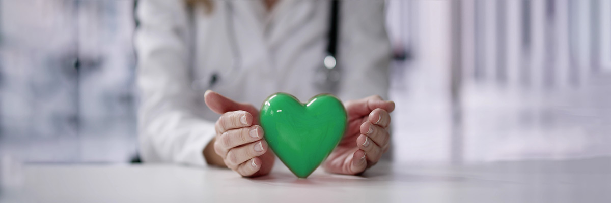 Una doctora abraza con sus manos un corazón verde